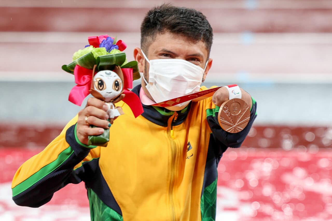 Petrúcio posa com a medalha de bronze. ele usa máscara e segura um buque de flores