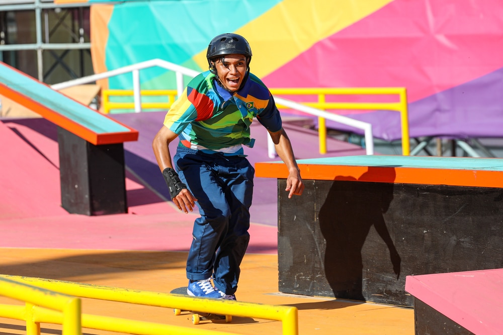 Matheus Theixeira em cima do skate. Ele pega impulso para tentar uma manobra. O atleta do Time Brasil veste uma calça azul e camiseta estampada. Rosário 2022