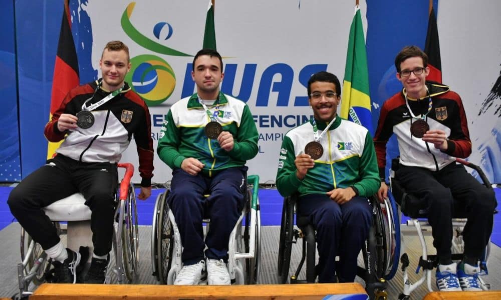 Kevin e os demais medalhistas do sabre posam para foto segurando as medalhas. Os 4 estão em suas cadeiras de rodas