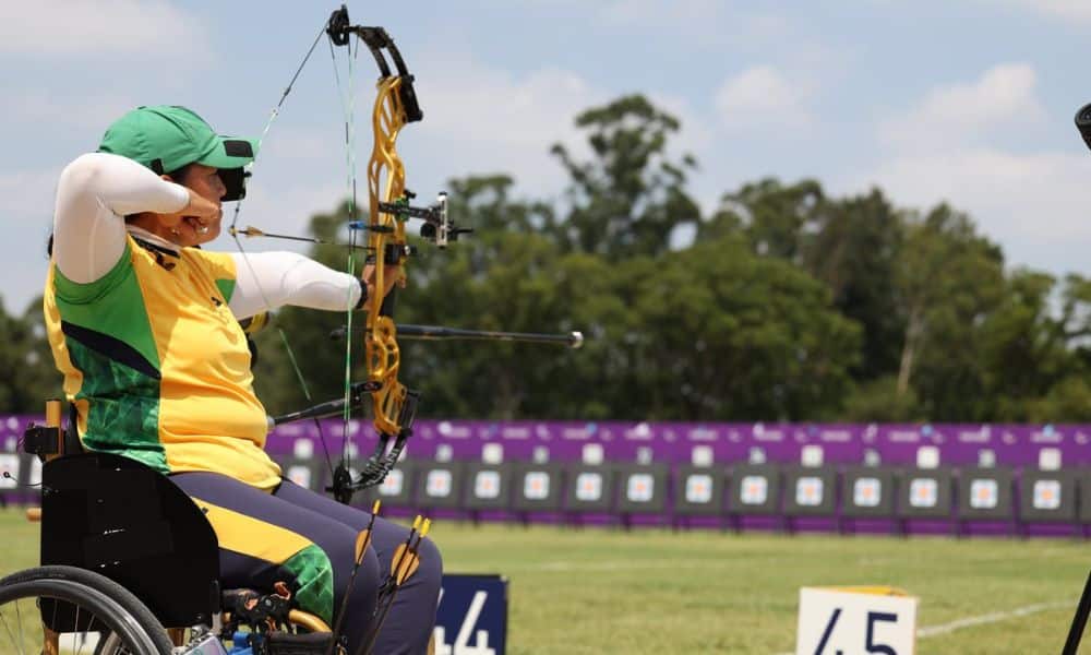 Brasil no tiro com arco: Jane karla dispara flecha. Ela está em uma cadeira de rodas e dispara em direção a uma série de alvos
