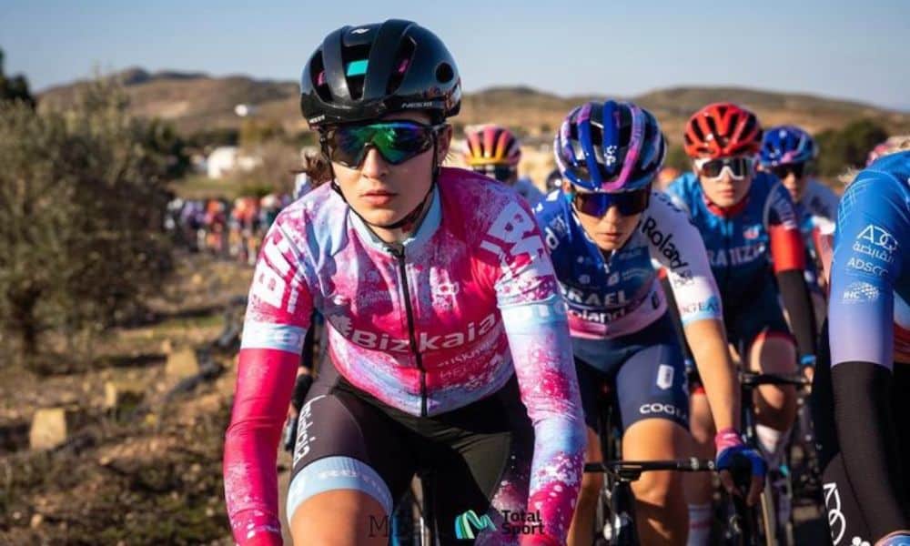 Ana Vitória Magalhães compete em prova de ciclismo estrada. Ela usa o uniforme cor de rosa de sua equipe