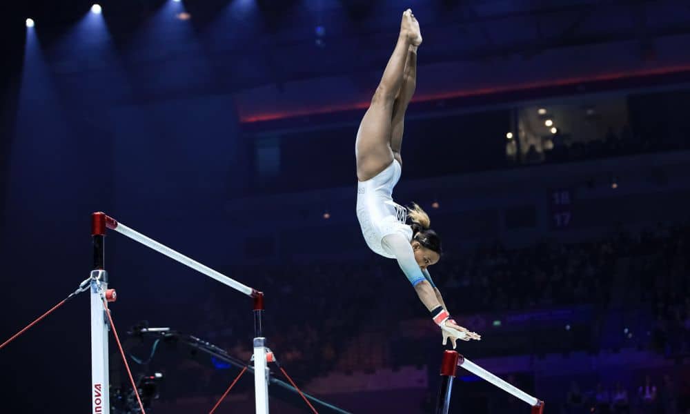 Rebeca Andrade voando entre as barras assimétricas com um salto pak mas