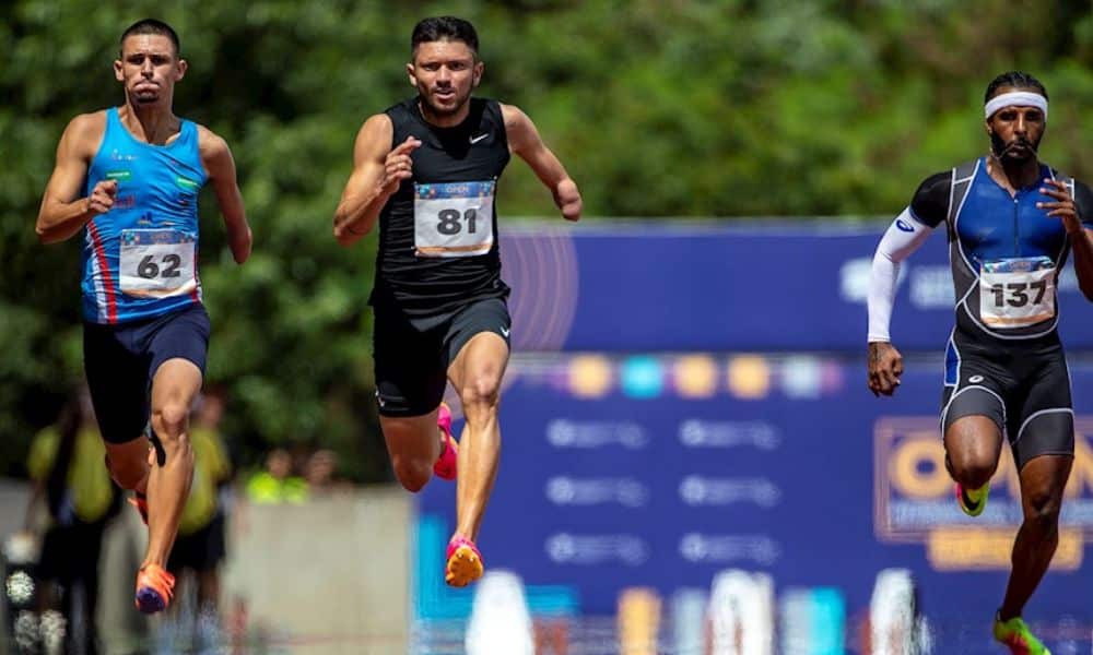 Mas - Petrúcio corre entre dois atletas. Ele veste shorts e regata pretas
