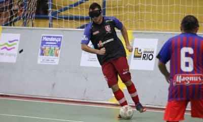 Atleta da Apadevi enquanto conduz a bola no Regional Nordeste de futebol de cegos. Ele veste shorts vermelho e camiseta preta