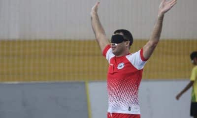 Derocy egue os braços para comemorar um gol da Escema no Regional Nordeste. Ele veste um uniforme vermelho e branco e uma venda preta