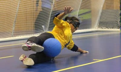 Na imagem, Jéssica estica as pernas na posição de chicote e faz a defesa durante treino; ela veste camisa de manga longa amarela da Seleção e calça preta. Foto: Renan Cacioli/ CBDV.