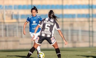 Em jogo do Brasileiro Feminino ao vivo, jogadora do cruzeiro conduz a bola enquanto é marcada por atleta do Santos