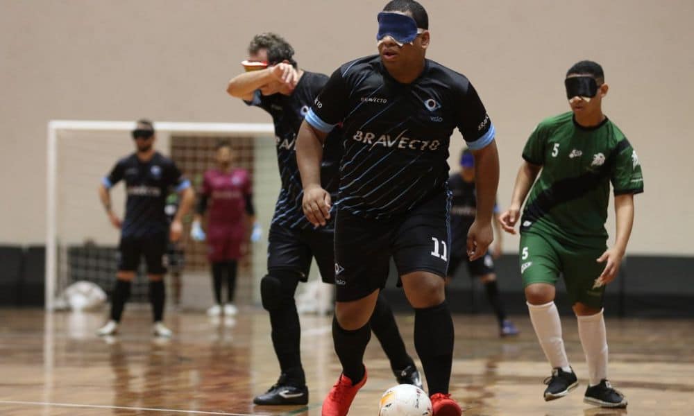 Dudu, que é preto e usa cabelo raspado em curto, conduz a bola, que está dominada em seu pé esquerdo. Ele veste uniforme preto com detalhes em azul, do INV (Renan Cacioli/ CBDV)