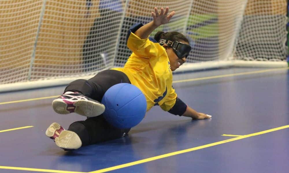 Jéssica estica as pernas na posição de chicote e faz a defesa durante treino; ela veste camisa de manga longa amarela da Seleção e calça preta (Renan Cacioli/ CBDV)