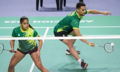 Fabrício Farias e Jaqueline Lima em quadra no Challenge do México de badminton. Ambos vestem shorts pretos e camisetas verdes. Fabrício ataca a peteca com a raquete
