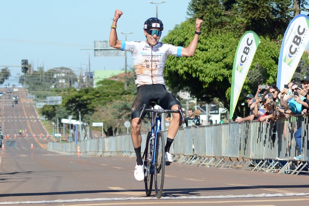 Na imagem, Caio Godoy comemorando em cima de sua bicicleta na linha de chegada.