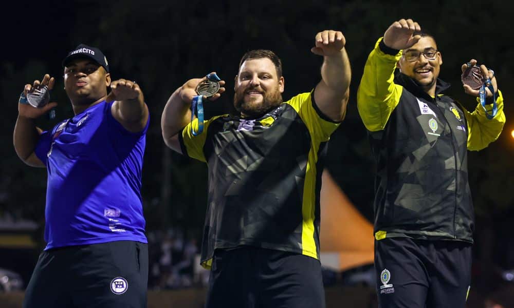Atletas do arremesso de peso posam para foto. Eles seguram a medalha em cima do ombro, brincando como se fosse o implemento da prova