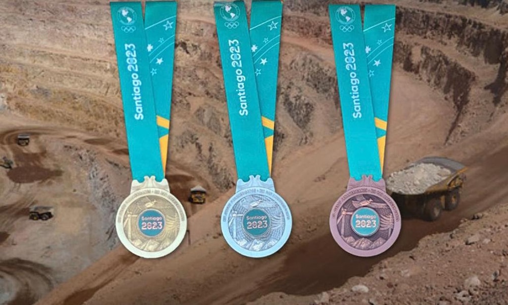 Na imagem, as medalhas dos Jogos Pan-Americanos de Santiago 2023, com uma mineradora ao fundo.