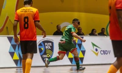 Na imagem, o ala Léo, da Agafuc, que veste uniforme predominantemente verde, sai vibrando após marcar seu gol entre dois adversários do CFCP, que usam camisa laranja.