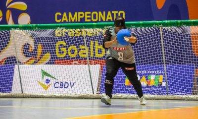 Jéssica Vitorino em ação de arremessar a bola. Ela está sozinha na imagem e, fundo, há o o gol e a logo do Campeonato Brasileiro de goalball, sob um banner roxo (Foto: Taba Benedicto/CBDV)