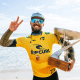 Filipe Toledo sorri, faz gesto com a mão e segura o troféu de campeão do Circuito Mundial de Surfe em frente ao mar