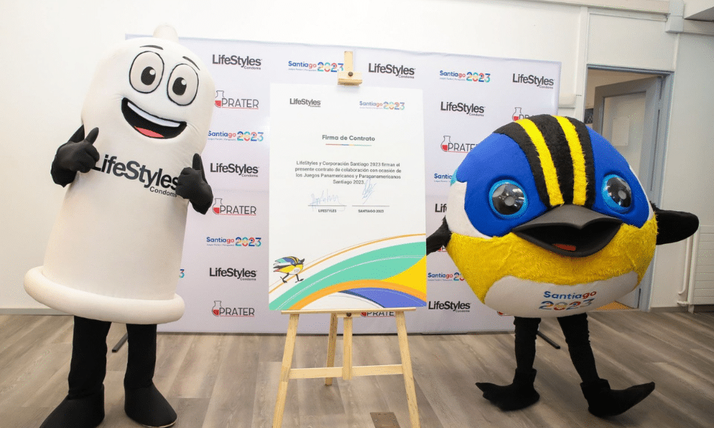 Personagem de preservativo e Piu, mascote de Santiago 2023, pousam para foto em frente ao contrato de assinatura de parceria entre Lifestyle e comitê organizador