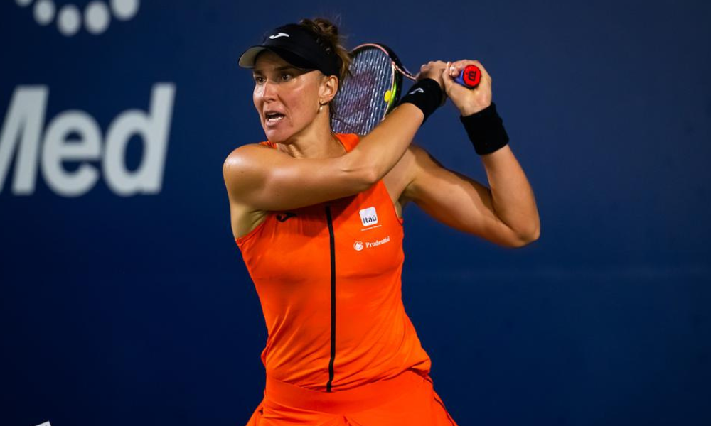 Bia Haddad veste laranja e usa viseira preta e faz movimento de rebatida, com a raquete na mão, ao fundo da cabeça, no WTA 1000 de Pequim. Ela jogou ao lado da russa Veronika Kudermetova