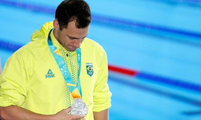 Léo de Deus olha para a medalha de prata, com a cabeça abaixada, em frente à piscina dos Jogos Pan-Americanos