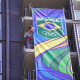 Trabalhador está na sacada de um prédio na Vila Pan-Americana ajustando uma plotagem com a marca do Time Brasil