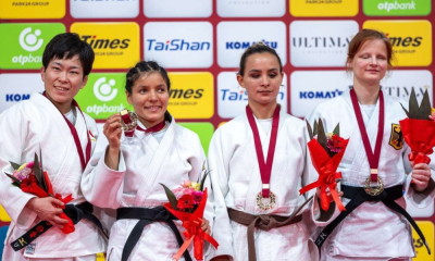 Rosi Andrade está com a medalha de bronze e segura um ramo de flores e está ao lado das outras três medalhistas de sua categoria no Grand Prix de Tóquio de judô paralímpico, em frente ao backdrop do evento