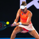 Bia Haddad, com uniforme laranja da Asics, rebate bola com backhand no Australian Open. Ela enfrenta Maria Timofeeva ao vivo