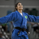 Mariana Silva usa quimono azul enquanto sorri de braços abertos após luta de judô