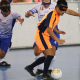 Vestindo uniforme laranja com detalhes em azul marinho, Angel conduz a bola enquanto passa pela marcação de três atletas do INV em partida do Regional Sul-Sudeste de futebol de cegos. Foto: Renan Cacioli/ CBDV.