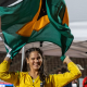 Wanna Brito sorri e segura a bandeira do Brasil após medalha de ouro no lançamento de club no Mundial de Kobe