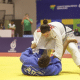 Alana Maldonado está de kimono branco, em pé, inclinada para frente, enquanto segura a outra atleta, que está de kimono azul e deitada de costas no tatame.