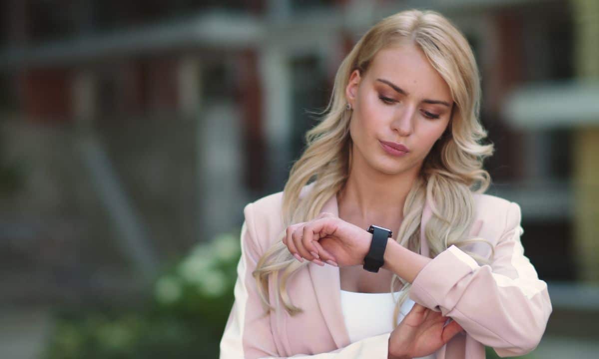 Pessoa olhando o relógio ou celular, em ambiente de trabalho ou casa, com expressão de indecisão sobre treinar.