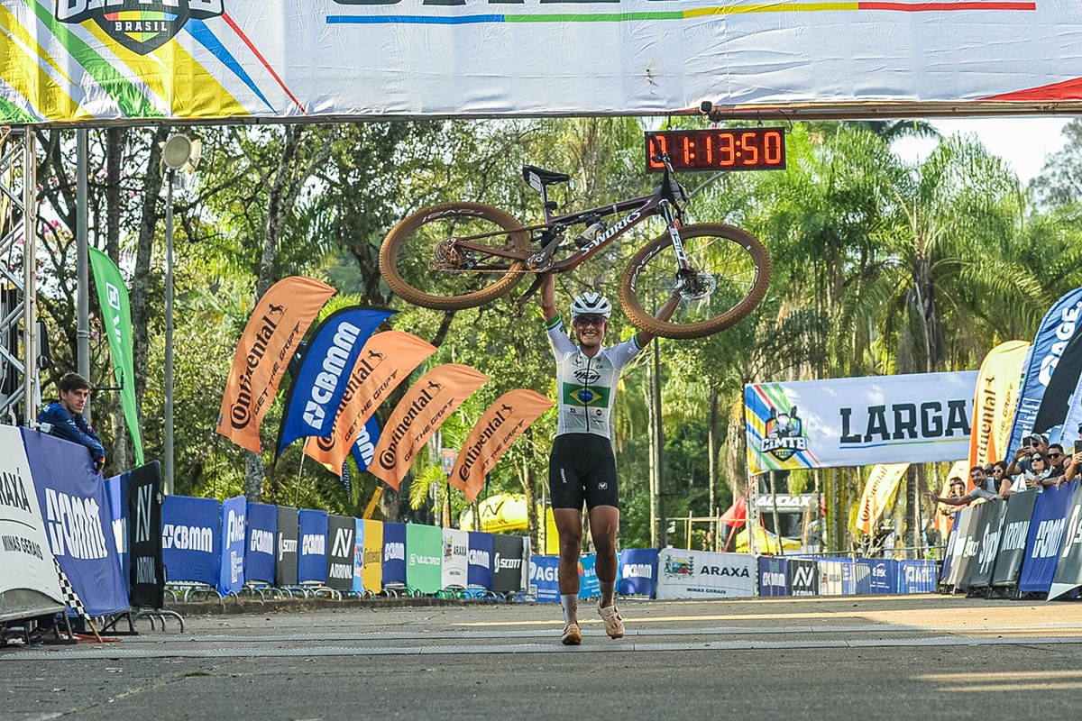 Na imagem, Karen Olimpio comemorando com sua bicicleta na linha de chegada.