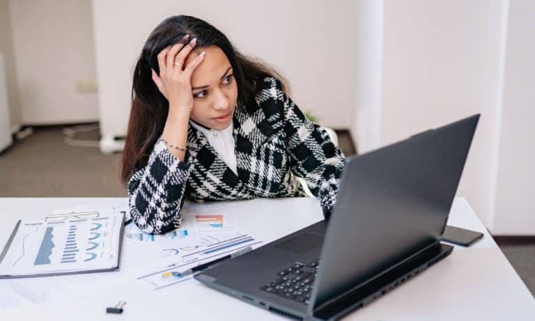 Pessoa sentada com expressão de esgotamento mental, cercada por trabalho e estímulos digitais.