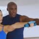 Pessoa aprende exercício de musculação com carga leve e orientação de profissional na academia.