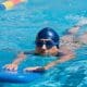 Pessoa nada crawl em piscina com destaque para a pernada e o alinhamento do quadril na água.