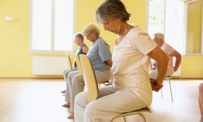 Pessoa com mais de 60 anos pratica yoga com apoio de uma cadeira