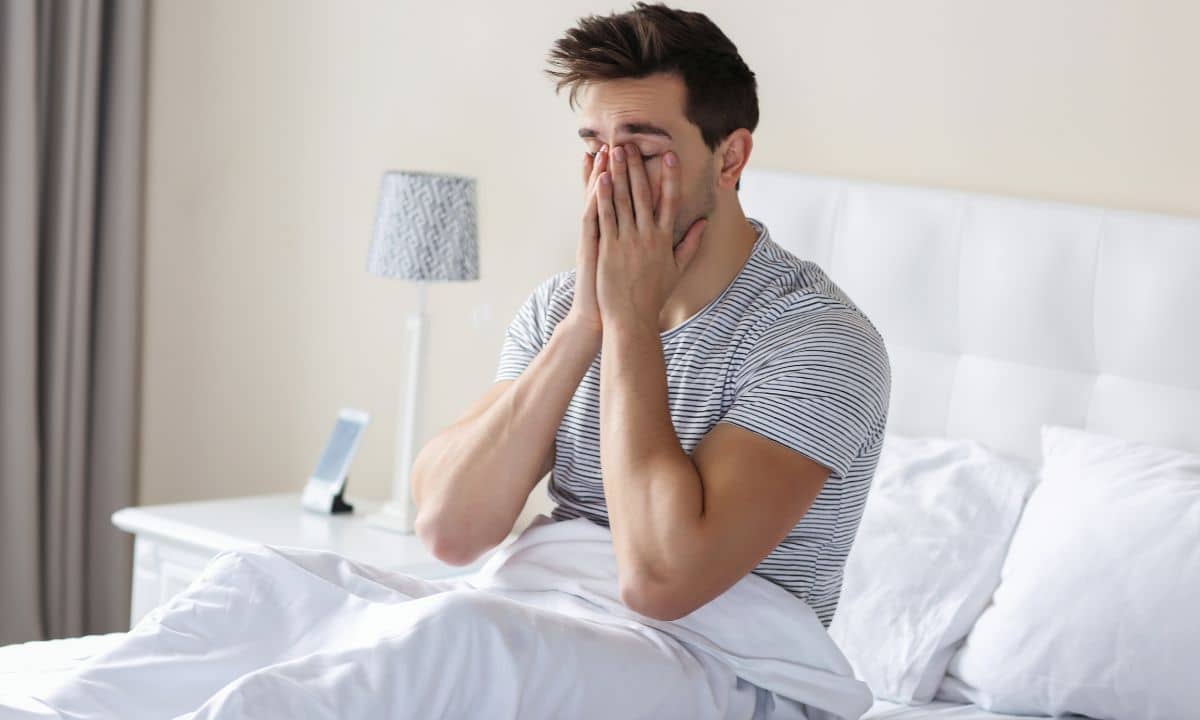 Pessoa acorda sonolenta e permanece sentada na cama enquanto entra luz pela janela.