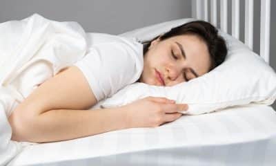 Pessoa dorme de lado com travesseiro apoiando cabeça e pescoço em posição confortável.