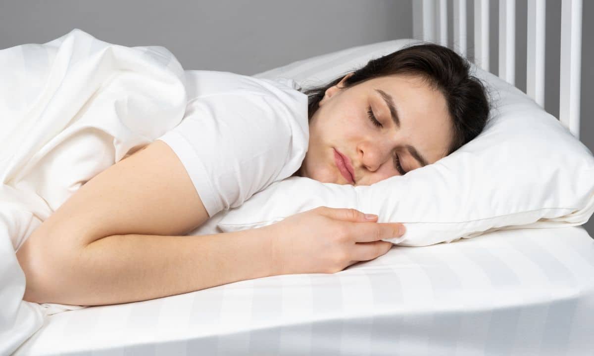 Pessoa dorme de lado com travesseiro apoiando cabeça e pescoço em posição confortável.