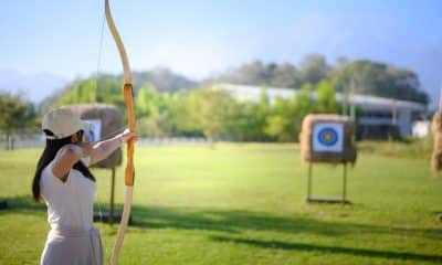 Pessoa pratica tiro com arco em posição de mira, com postura alinhada e braços sustentando o arco.
