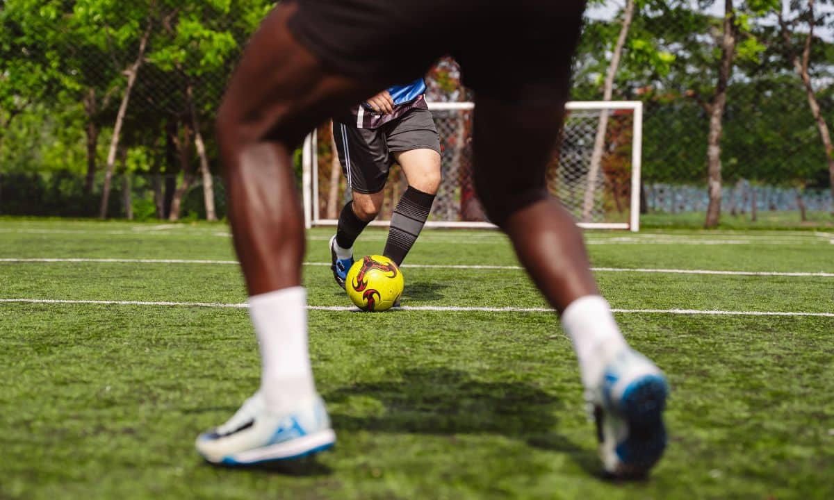 ogadores disputam uma partida de futebol sobre campo de grama sintética.