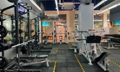 Foto horizontal mostrando, no mesmo enquadramento, uma máquina de musculação e um suporte com halteres